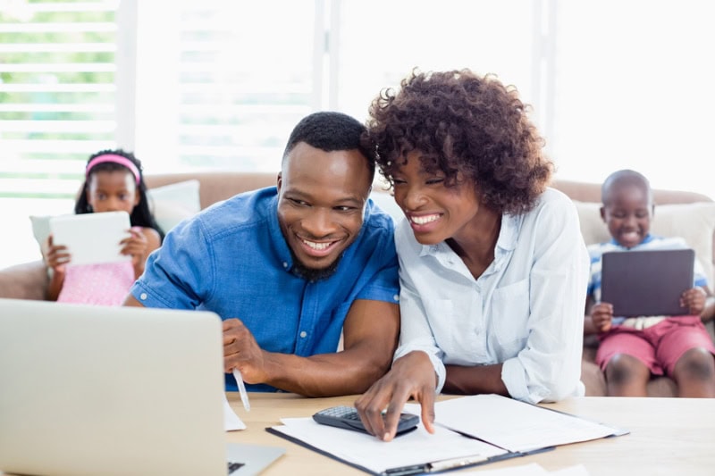 Happy married couple watching videos on things you might not know about air conditioners with children on couch behind them.