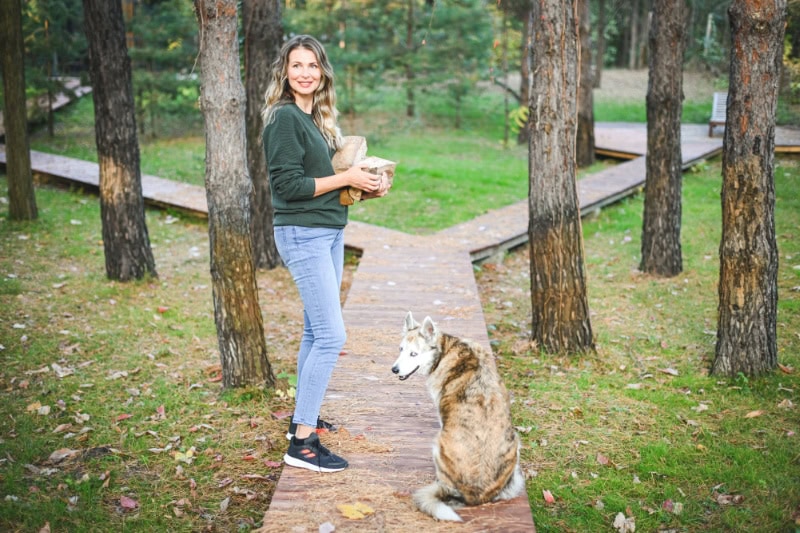 Female homeowner collecting firewood with dog to represent when it is time to buy a new furnace.