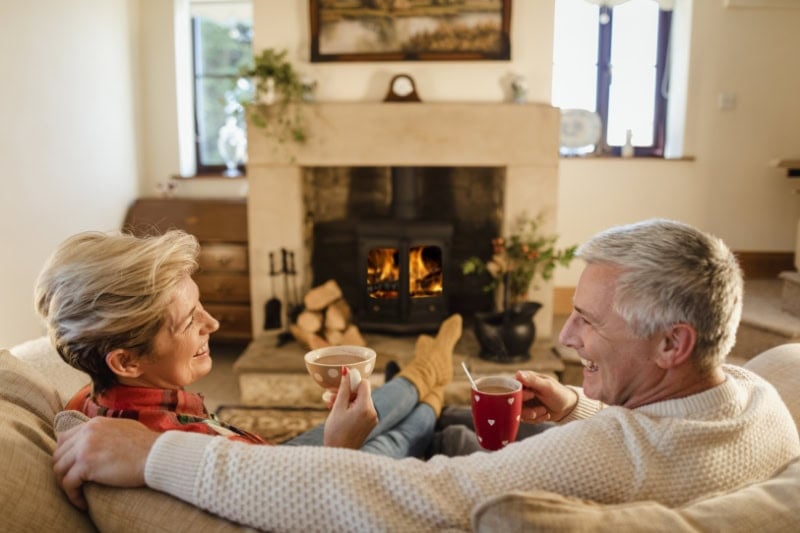 Older married couple enjoying coffee in front of fireplace during extreme cold weather in Hudson, MA.