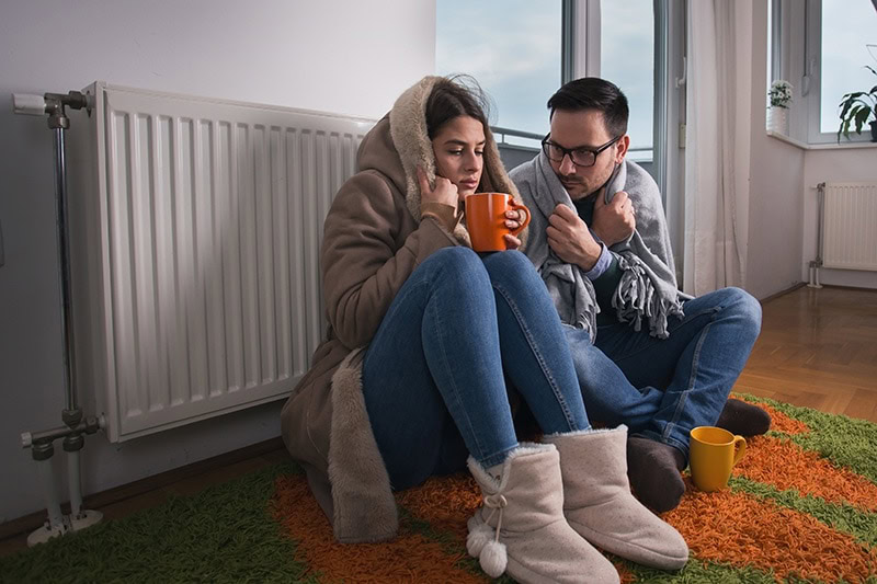 Couple freezing in front of a radiant floor heating system to represent when you know you need a new furnace.