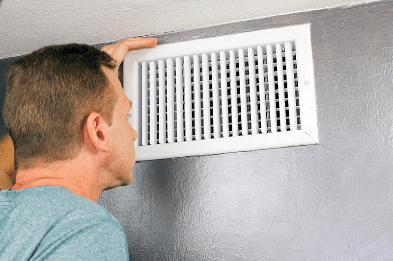 HVAC technician in front of wall vent trying to figure out if air conditioner is blowing out hot air.