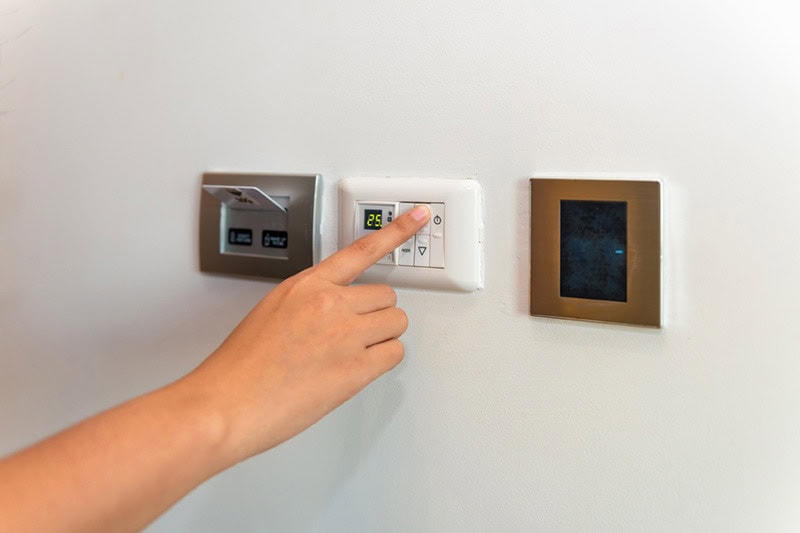 Homeowner adjusting thermostat to represent information on whether a heat pump or furnace is better.