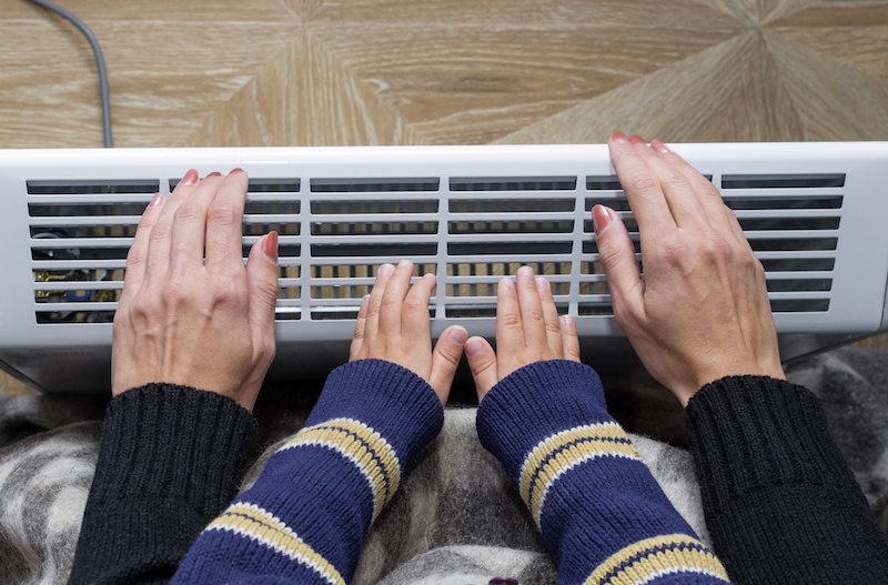 Mother and son heating up a hand in front of an electric heater. Modern electric heater
