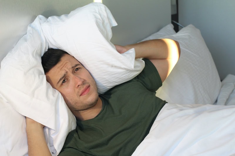 Frustrated man covering his ears with pillow.